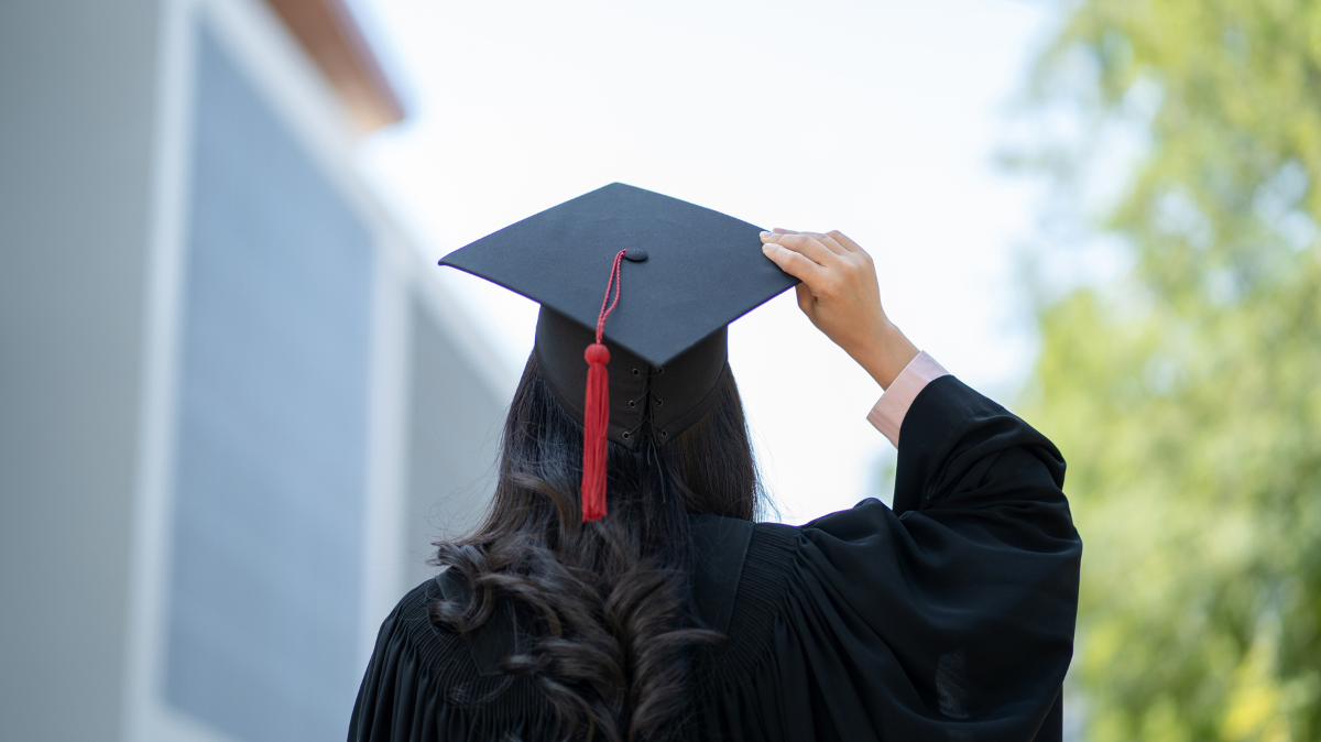 Back of woman wearing graduation outfit holding graduation cap