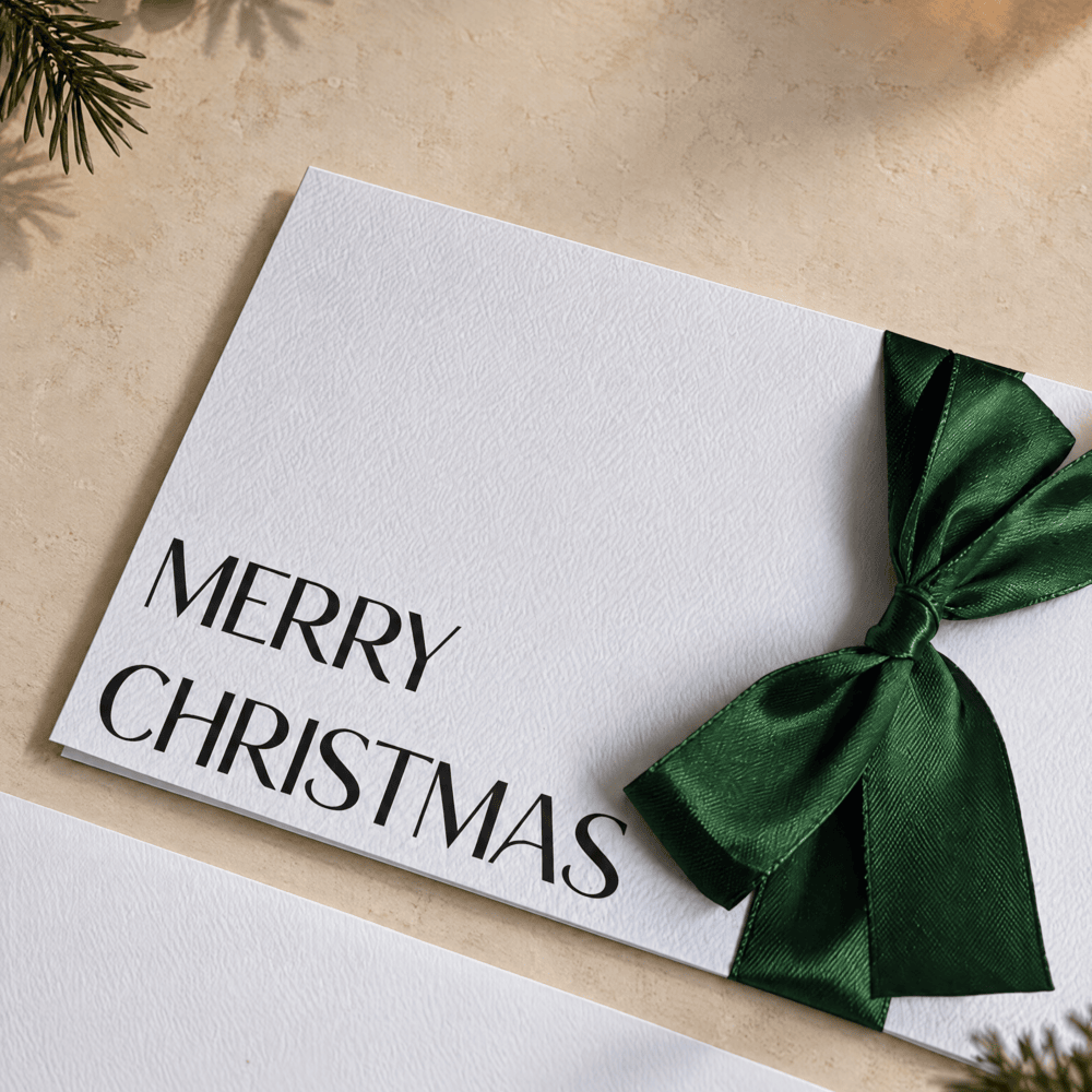 Close up of christmas card with merry christmas printed in black ink and a green satin ribbon