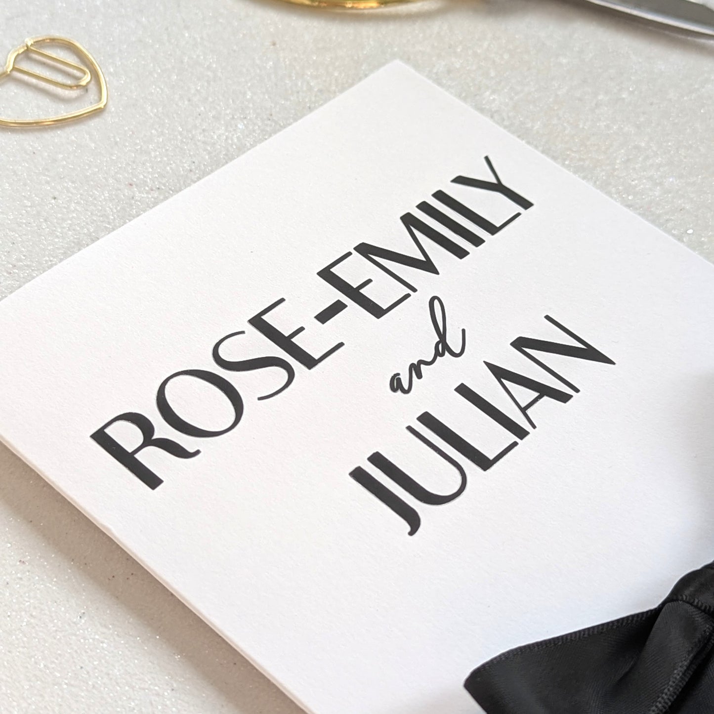 Close up of White wedding cards congratulations with money holder personalised with "Rose-Email and Julian" matte black names with a black ribbon