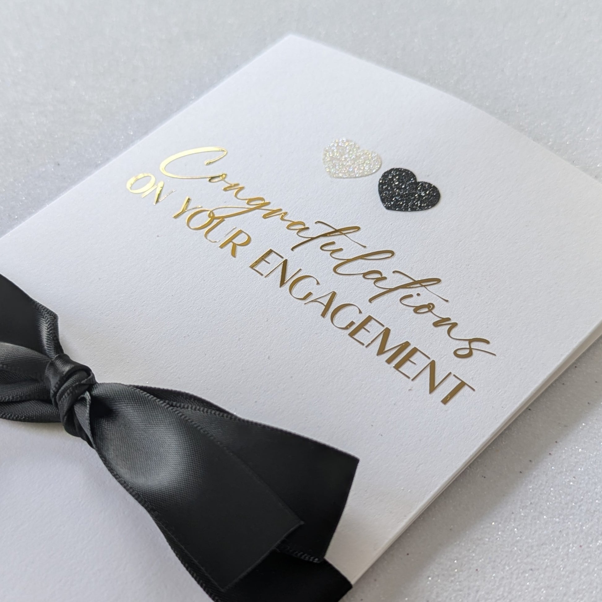 Close up of Congratulations on your engagement gift envelope with black and white glitter hearts and black satin ribbon