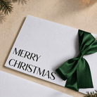 Close up of christmas card with merry christmas printed in black ink and a green satin ribbon