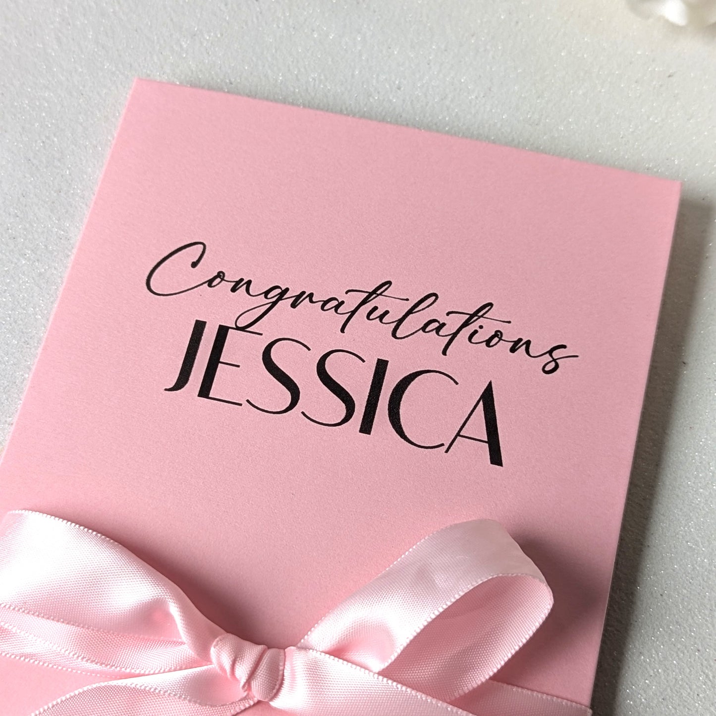 Close up of Personalised pink bridal shower or baby shower gift card holder greeting card envelope with congratulations Jessica printed on the front with pink satin ribbon