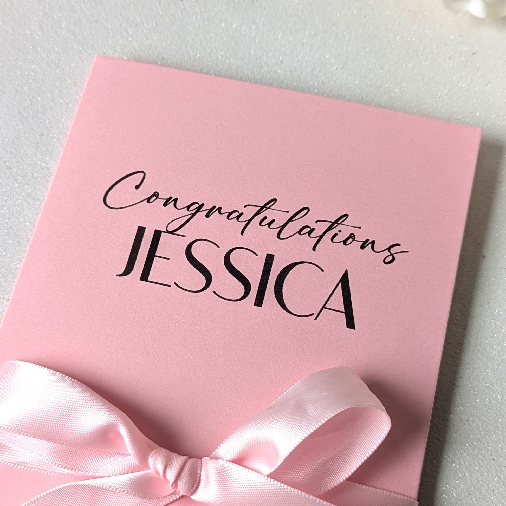Close up of Personalised pink bridal shower or baby shower gift card holder greeting card envelope with congratulations Jessica printed on the front with pink satin ribbon